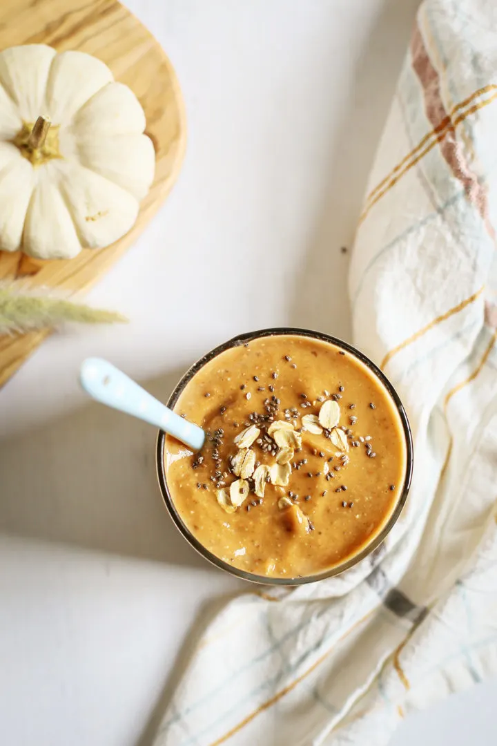 overhead photo of a glass full of a pumpkin smoothie with a chia seed and oatmeal garnish on top