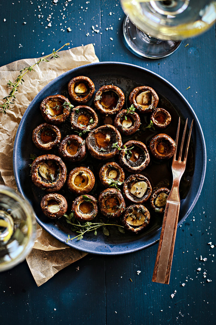 overhead photo of a blue plate of roasted portobello mushrooms with balsamic, garlic, and thyme on a blue table