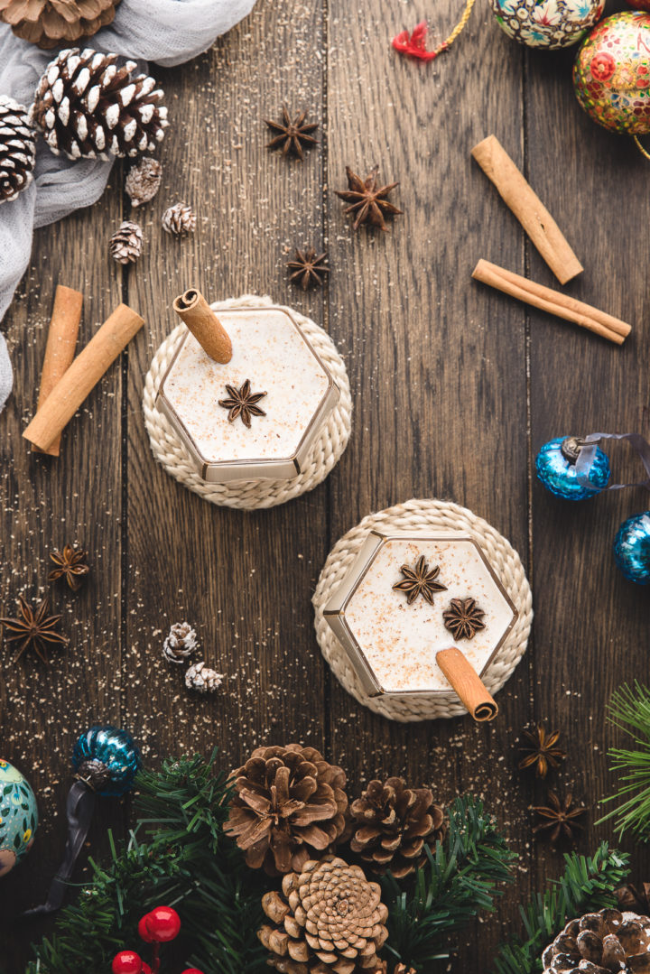 overhead shot of a wooden table with christmas decor and two glasses of spiked eggnog