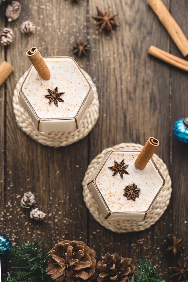 overhead photo of spiked eggnog with cinnamon stick garnish in two glasses on a wooden table
