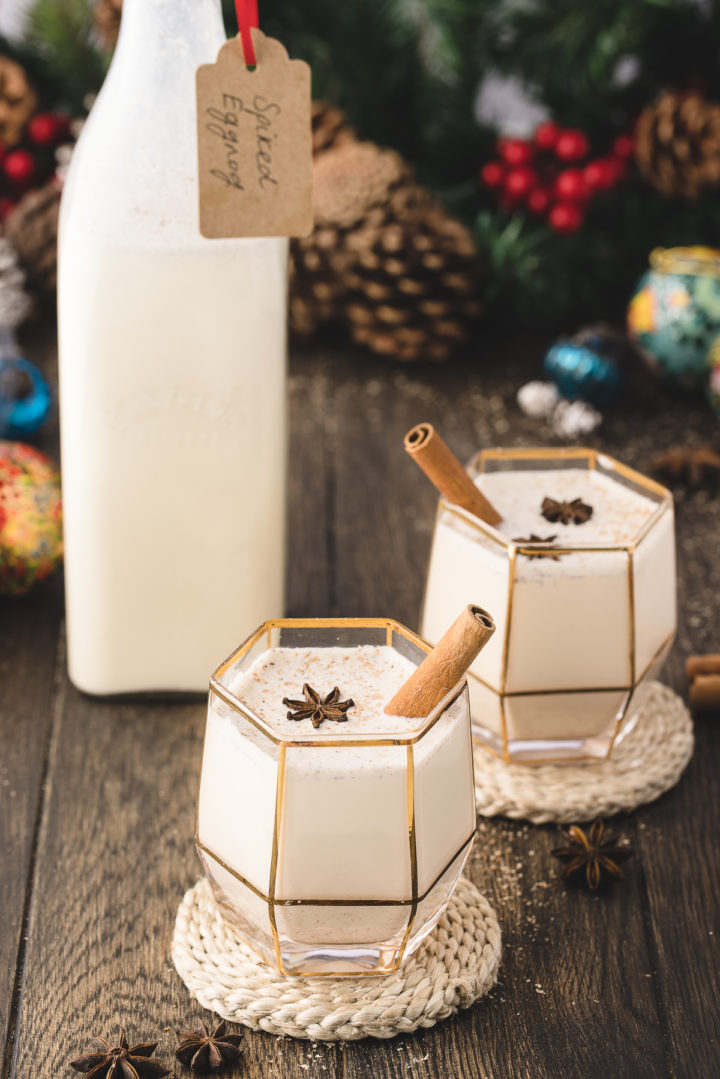 photo of two glasses of spiked eggnog with a bottle of eggnog on a table set for christmas