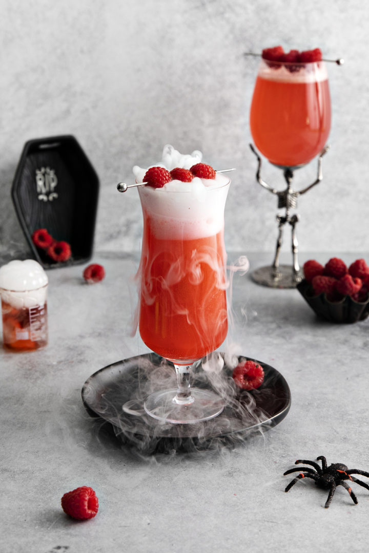 photo of a halloween cocktail with gin and raspberries served with dry ice to create a smoke effect