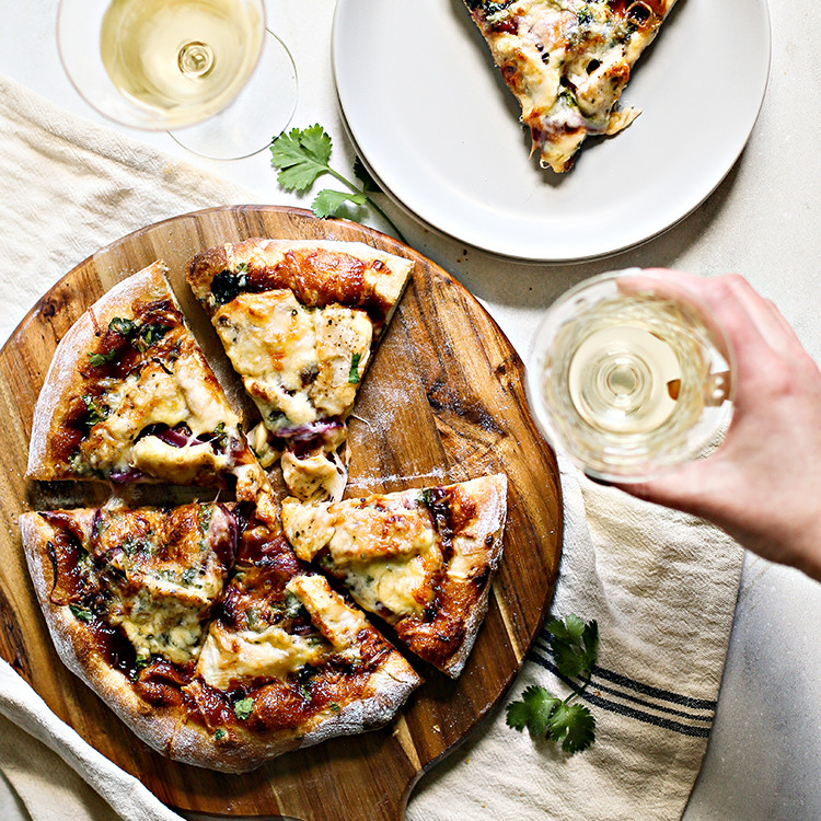 woman holding a glass of white wine next to a bbq chicken pizza