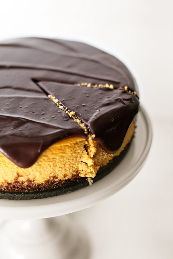 photo of a pumpkin cheesecake on a white cake stand with one slice of cheesecake cut