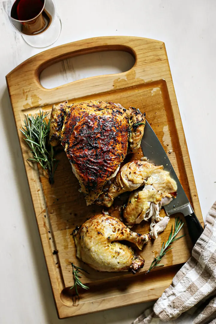 photo of rosemary roasted chicken cut up on a cutting board with a chef's knife kitchen towel, and glass of red wine
