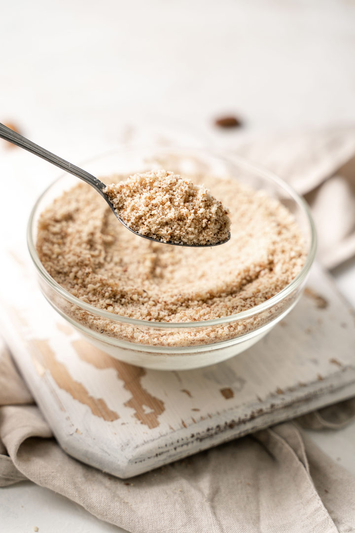 photo of a spoonful of diy almond meal on a wooden cutting board