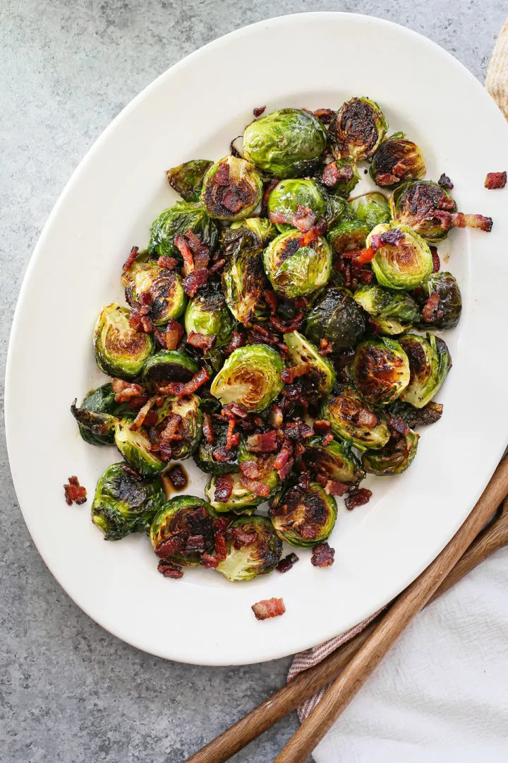 roasted brussels sprouts with bacon and balsamic on a white platter with wooden serving spoons