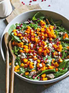 photo of butternut squash salad in a white bowl with wooden serving spoons