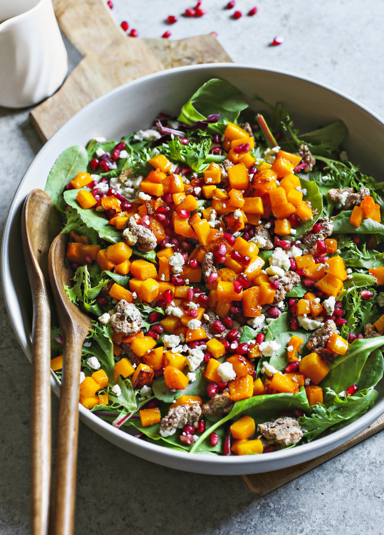 photo of butternut squash salad in a white bowl with wooden serving spoons