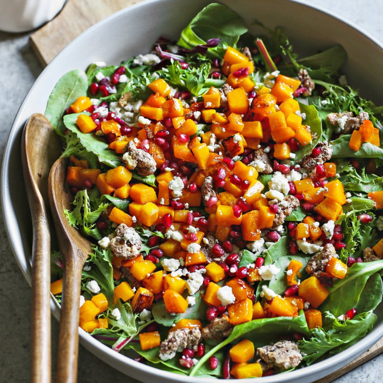 photo of butternut squash salad in a white bowl with wooden serving spoons