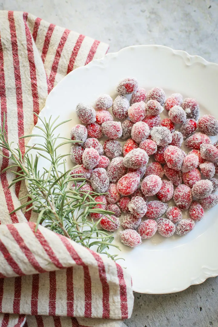 overhead photo of sugared cranberries on a white plate on a grey table