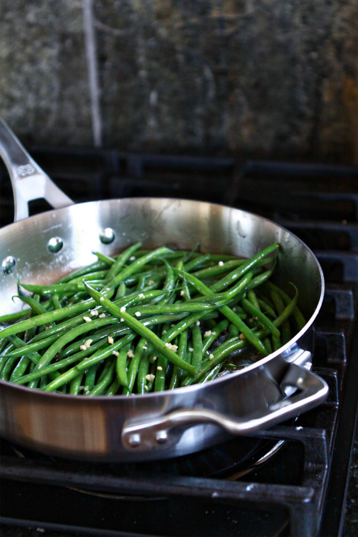photo of sautéed green beans being cooked in a stainless steel skillet on a gas stove