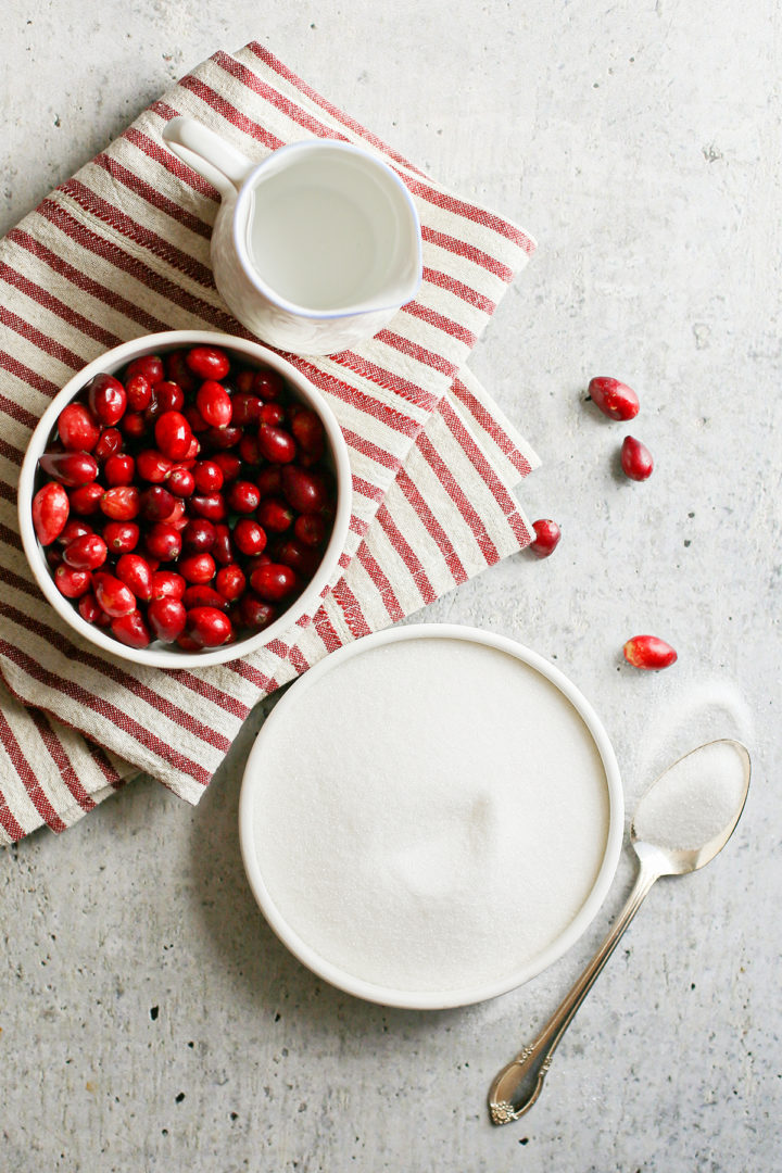 photo of fresh cranberries in a white bowl next to a bowl of sugar