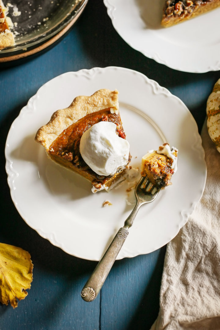 close up photo of a slice of pumpkin pie with whipped cream being eaten with a fork