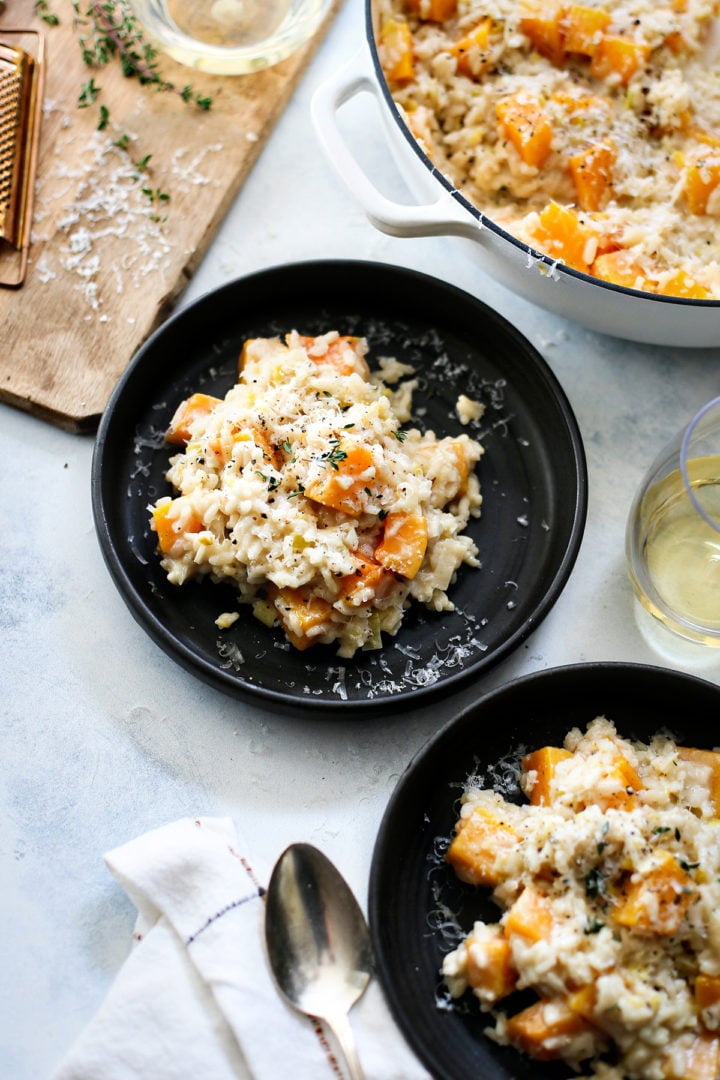 a table set with a pot of butternut squash risotto and two servings on black plates