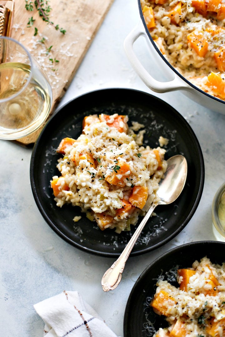 close up overhead photo of a plate of butternut squash risotto with a spoon and a glass of wine