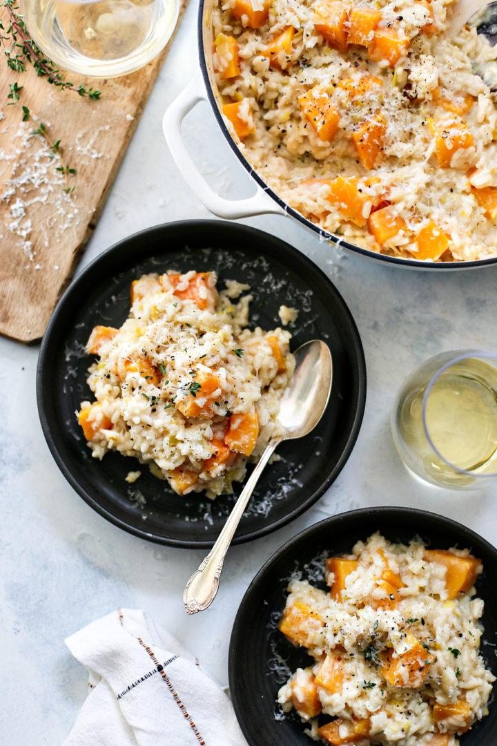 a pot of butternut squash risotto with two plate and a glass of white wine