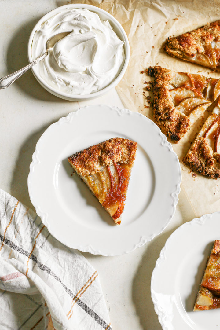 overhead photo of a table set with plates of pear galette and a bowl of whipped cream