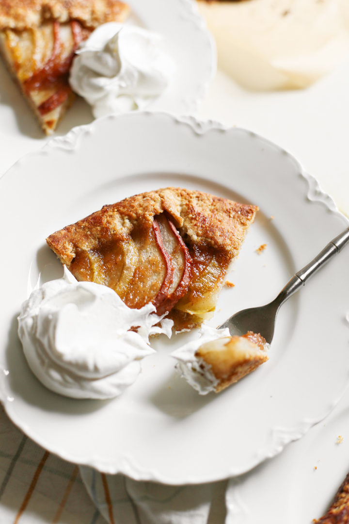 close up photo of a slice of pear galette on a plate with whipped cream and a fork