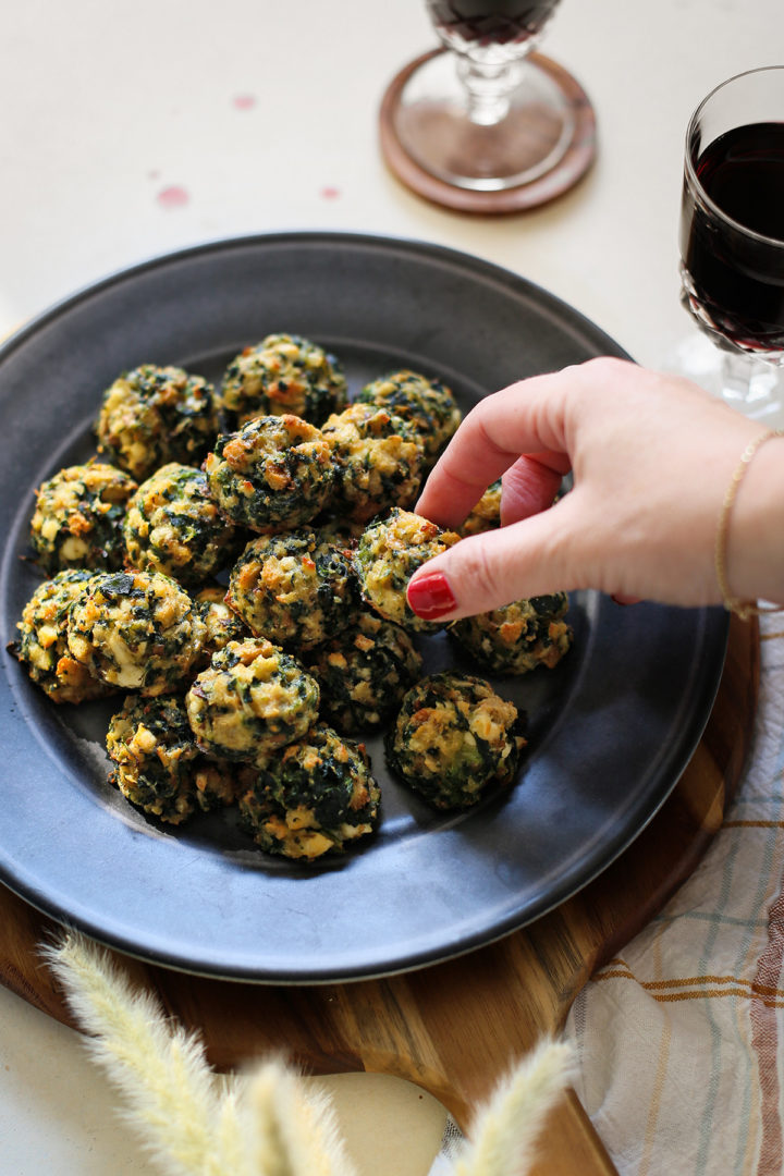 photo of a woman selecting a spinach ball appetizer off of a plate