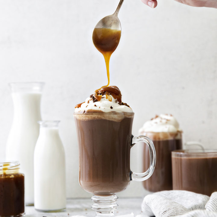 photo of salted caramel hot chocolate in a clear mug with caramel being drizzled on the top