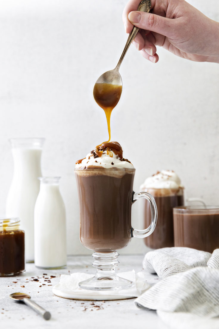 photo of salted caramel hot chocolate in a clear mug with caramel being drizzled on the top