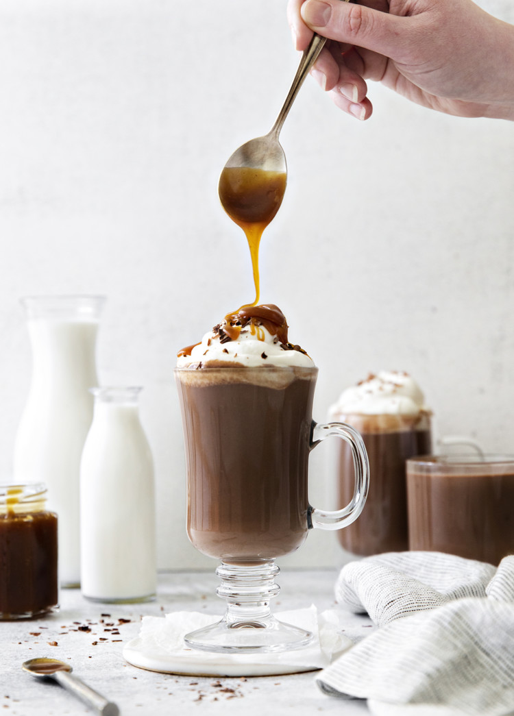 photo of salted caramel hot chocolate in a clear mug with caramel being drizzled on the top