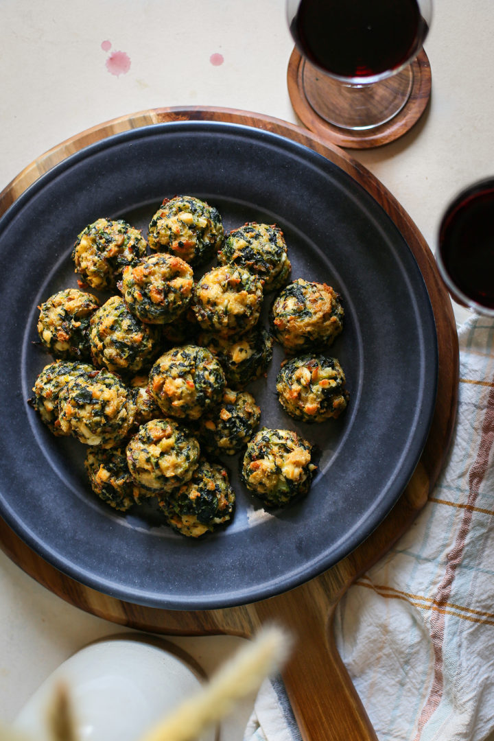 overhead photo of a plate of spinach balls on a table with two glasses of red wine