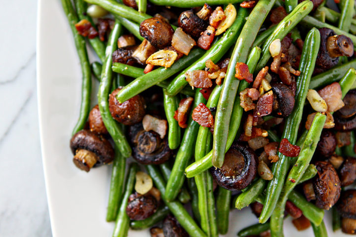 overhead photo of a white serving plate with sautéed green beans thanksgiving on a white marble counter