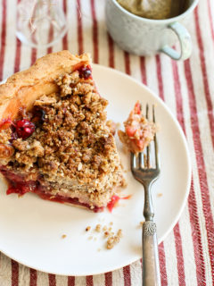 photo of a slice of apple cranberry pie with crumble topping on a white plate with a fork