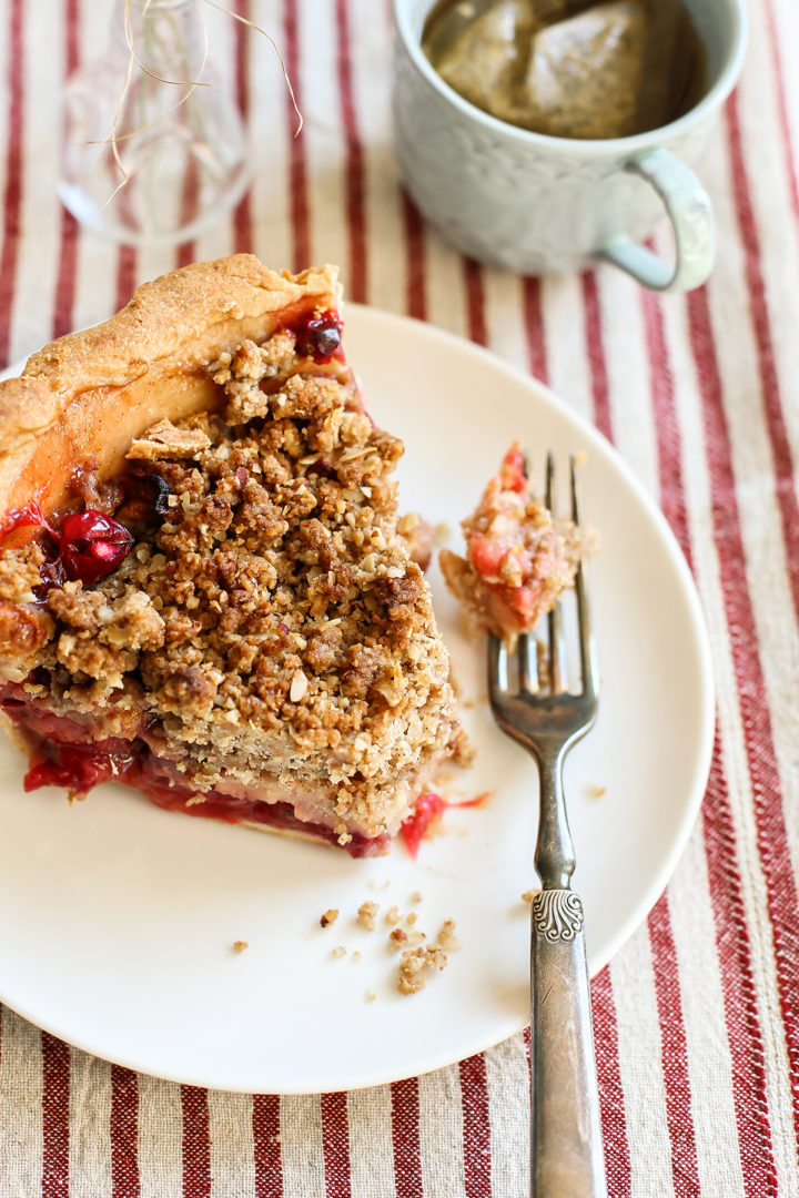 photo of a slice of apple cranberry pie with crumble topping on a white plate with a fork