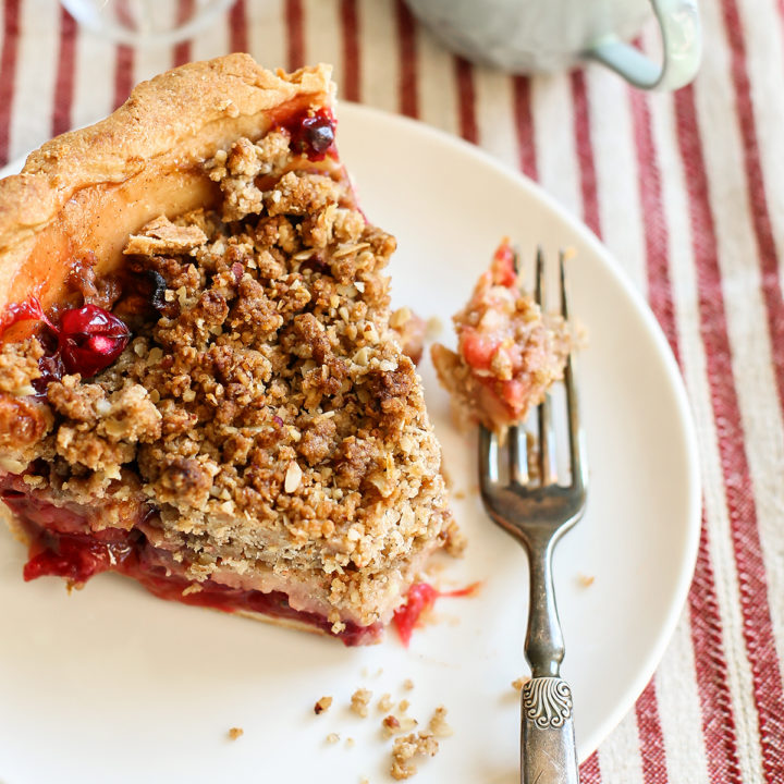 photo of a slice of apple cranberry pie with crumble topping on a white plate with a fork