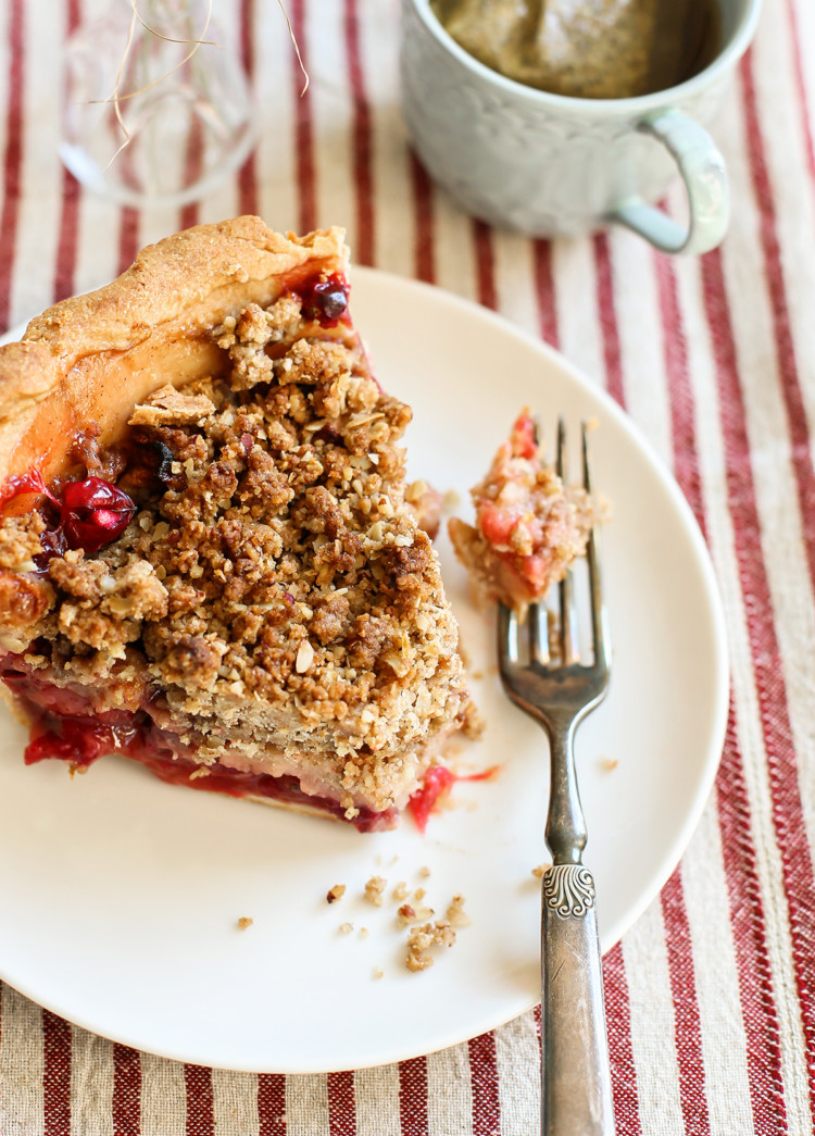 photo of a slice of apple cranberry pie with crumble topping on a white plate with a fork