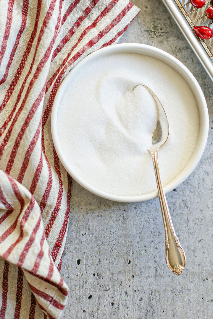 photo of granulated sugar in a white bowl with a spoon for use in this recipe for sugared cranberries