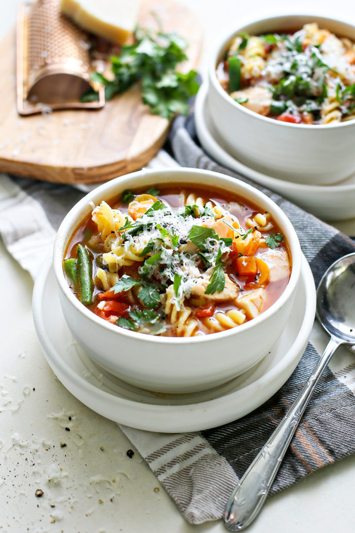 photo of turkey vegetable soup in a white bowl with a spoon and cloth napkin