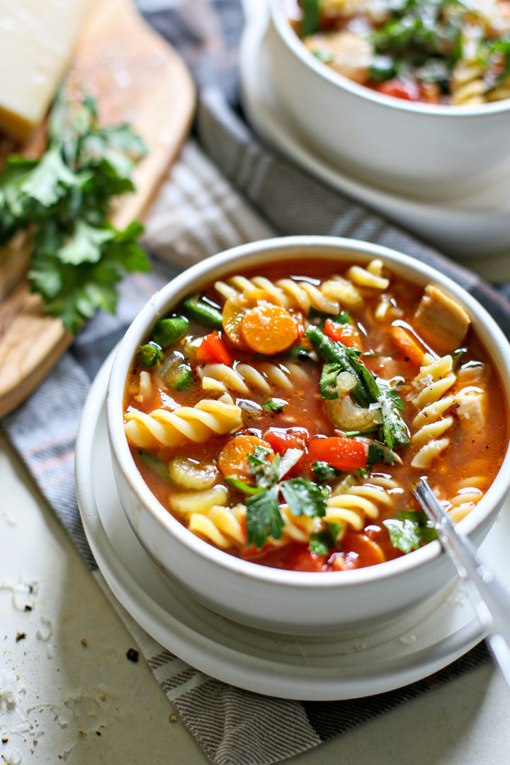 photo of a table set with two bowls of turkey vegetable soup with parsley and fresh parmesan