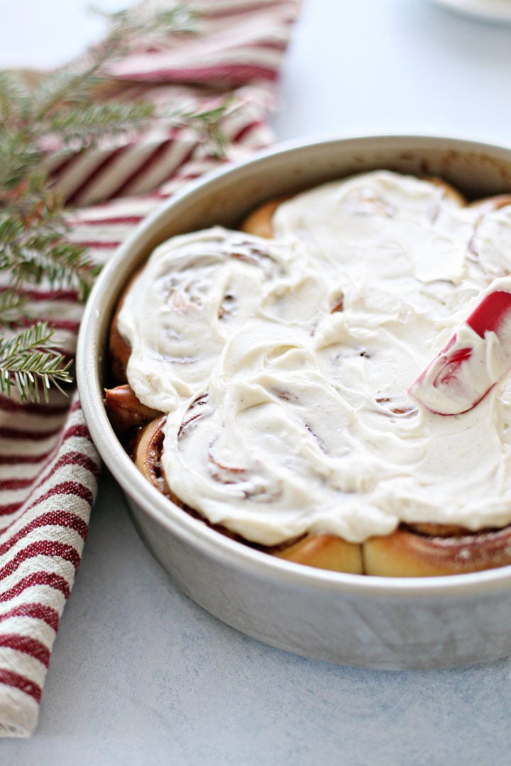 a pan of homemade cinnamon rolls with cream cheese cinnamon roll icing on a counter with a striped towel