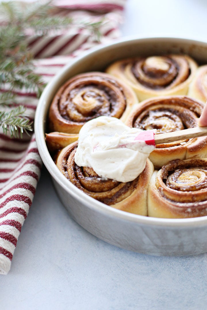 photo of homemade cinnamon roll icing being spread on baked cinnamon rolls