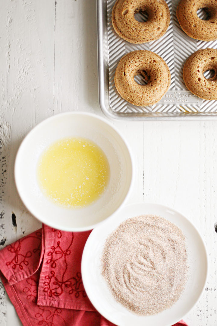 photo showing a batch of baked donuts on a baking sheet next to the ingredients to make cinnamon donuts