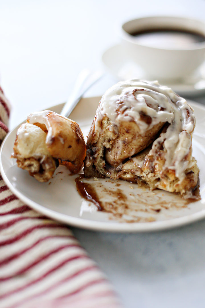 photo of a warm cinnamon roll on a plate with a mug of coffee