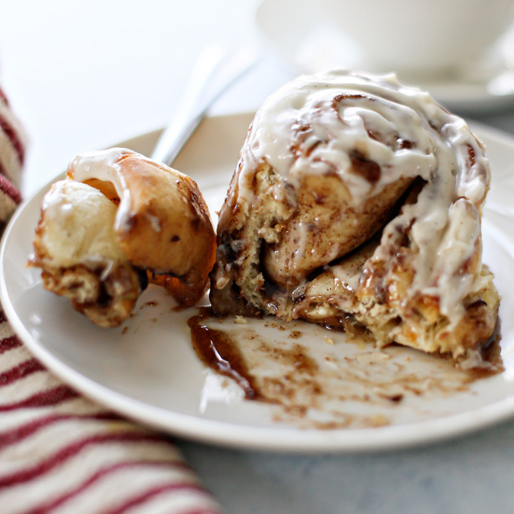 photo of a gooey cinnamon roll with bourbon cream cheese frosting on a white plate