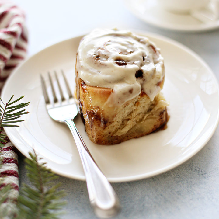 cinnamon roll with cream cheese frosting on a white plate with a fork