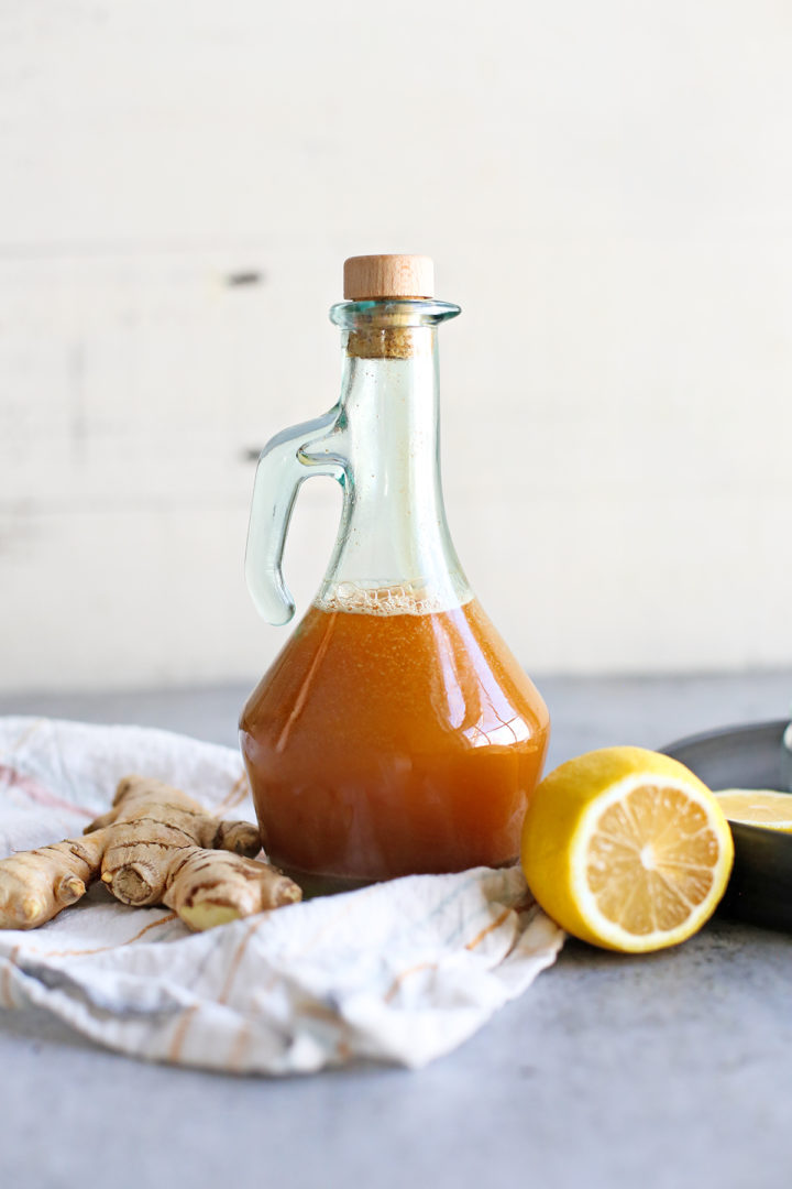 photo of homemade cough syrup in a jar next to fresh ginger and fresh lemon