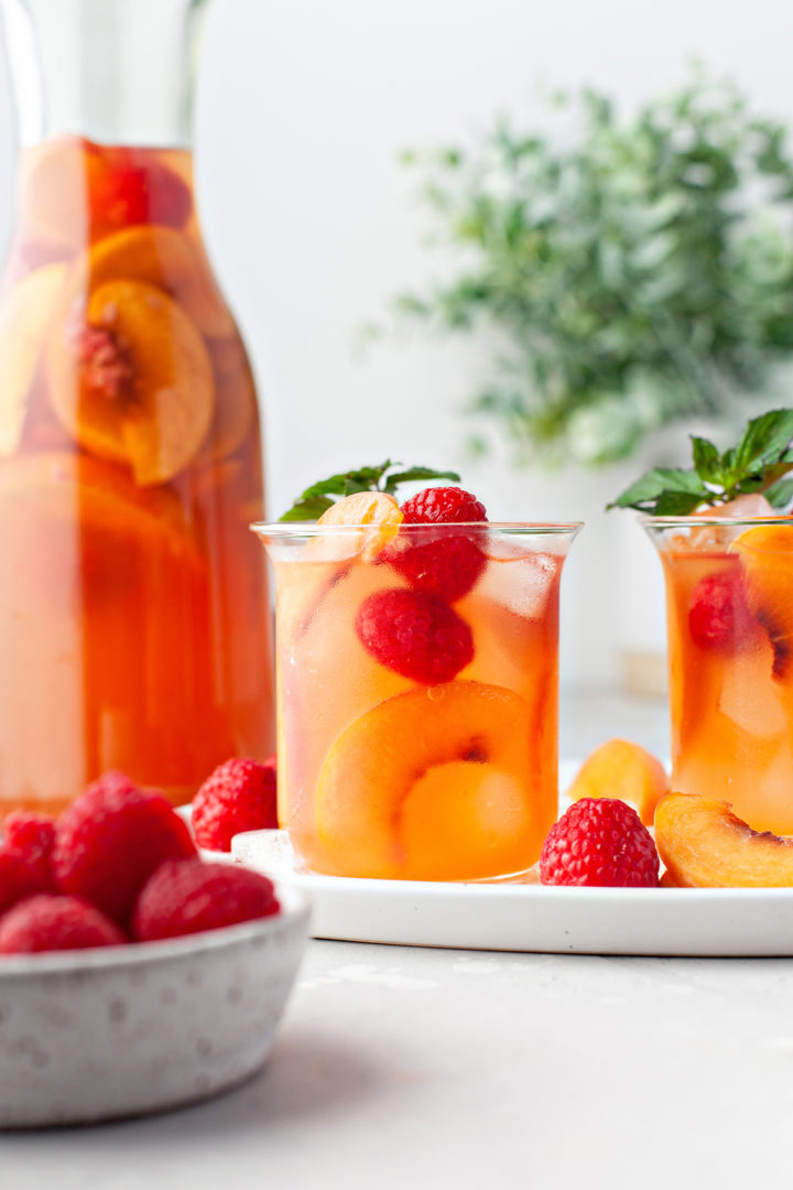 table set with a carafe of peach sangria and two glasses of sangria with peaches and raspberries