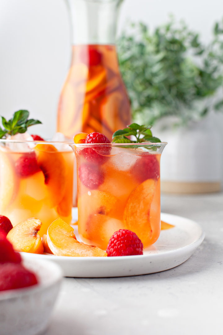 photo of peach sangria recipe in a glass garnished with raspberries and fresh mint