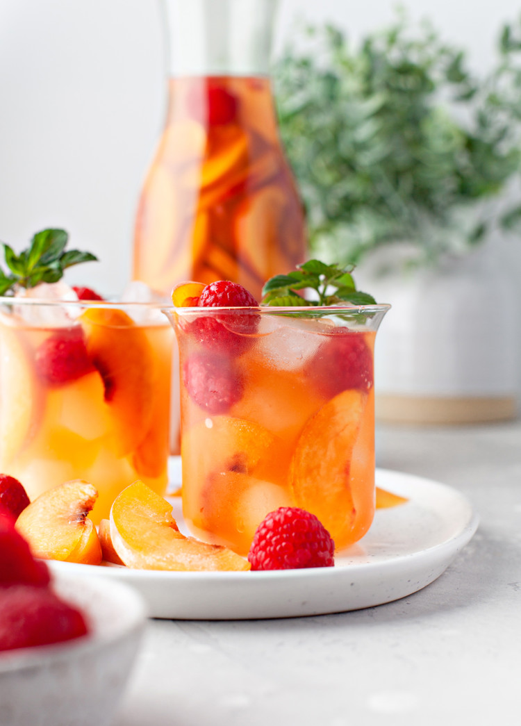 photo of peach sangria in a glass garnished with fresh raspberries and mint leaves