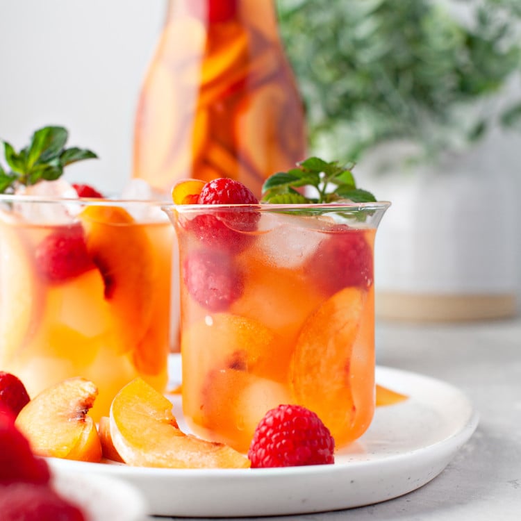 photo of peach sangria in a glass garnished with fresh raspberries and mint leaves