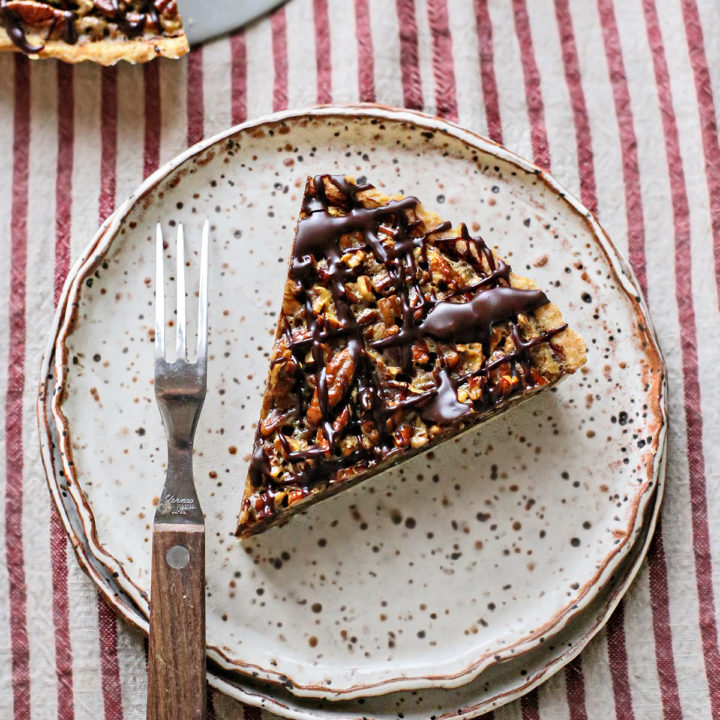 photo of a slice of chocolate pecan tart on a plate with a fork from this pecan tart recipe