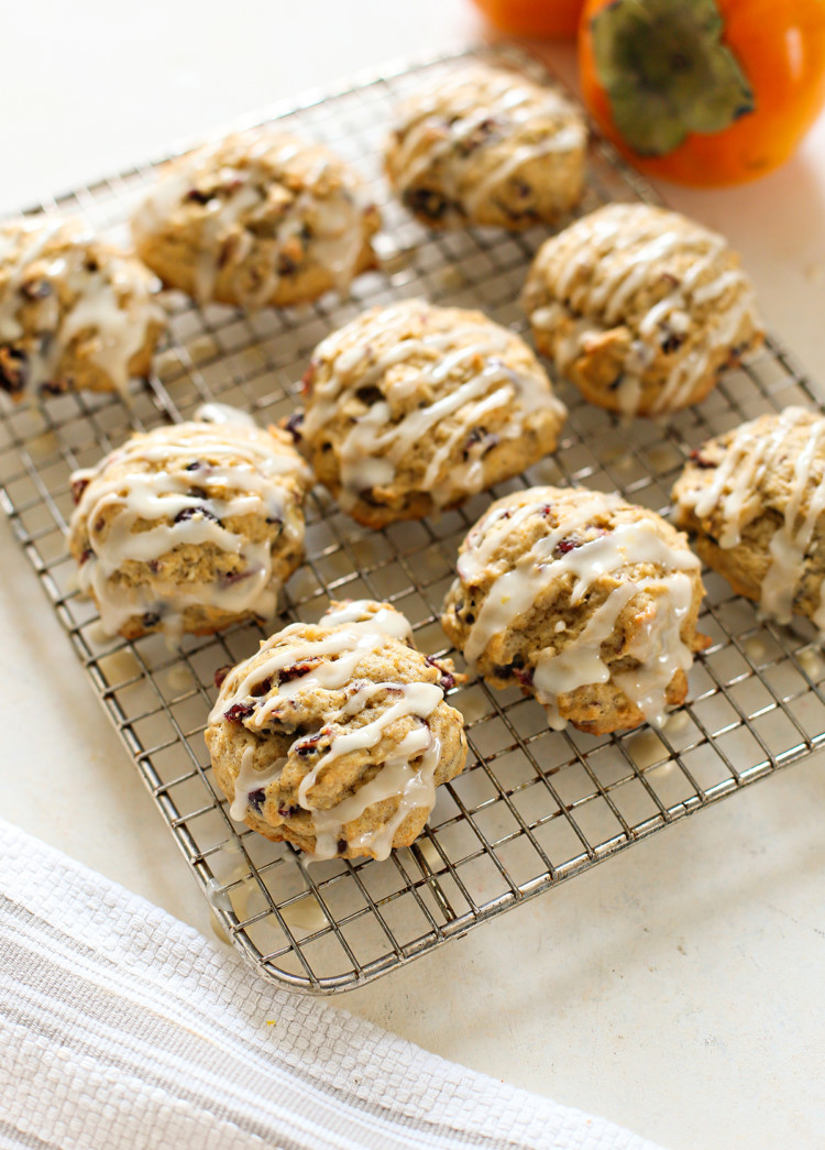 persimmon cookies drizzled with orange glaze on a wire rack with fresh persimmon in the background