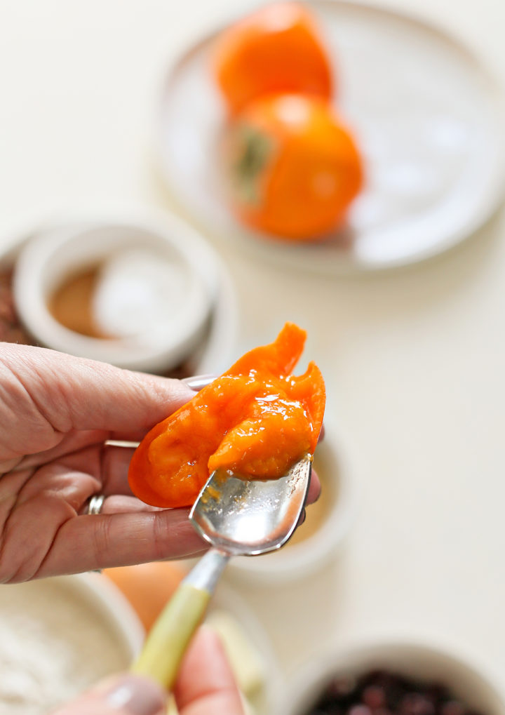 photo of a woman scooping persimmon pulp out of a hachiya persimmon to make persimmons cookies